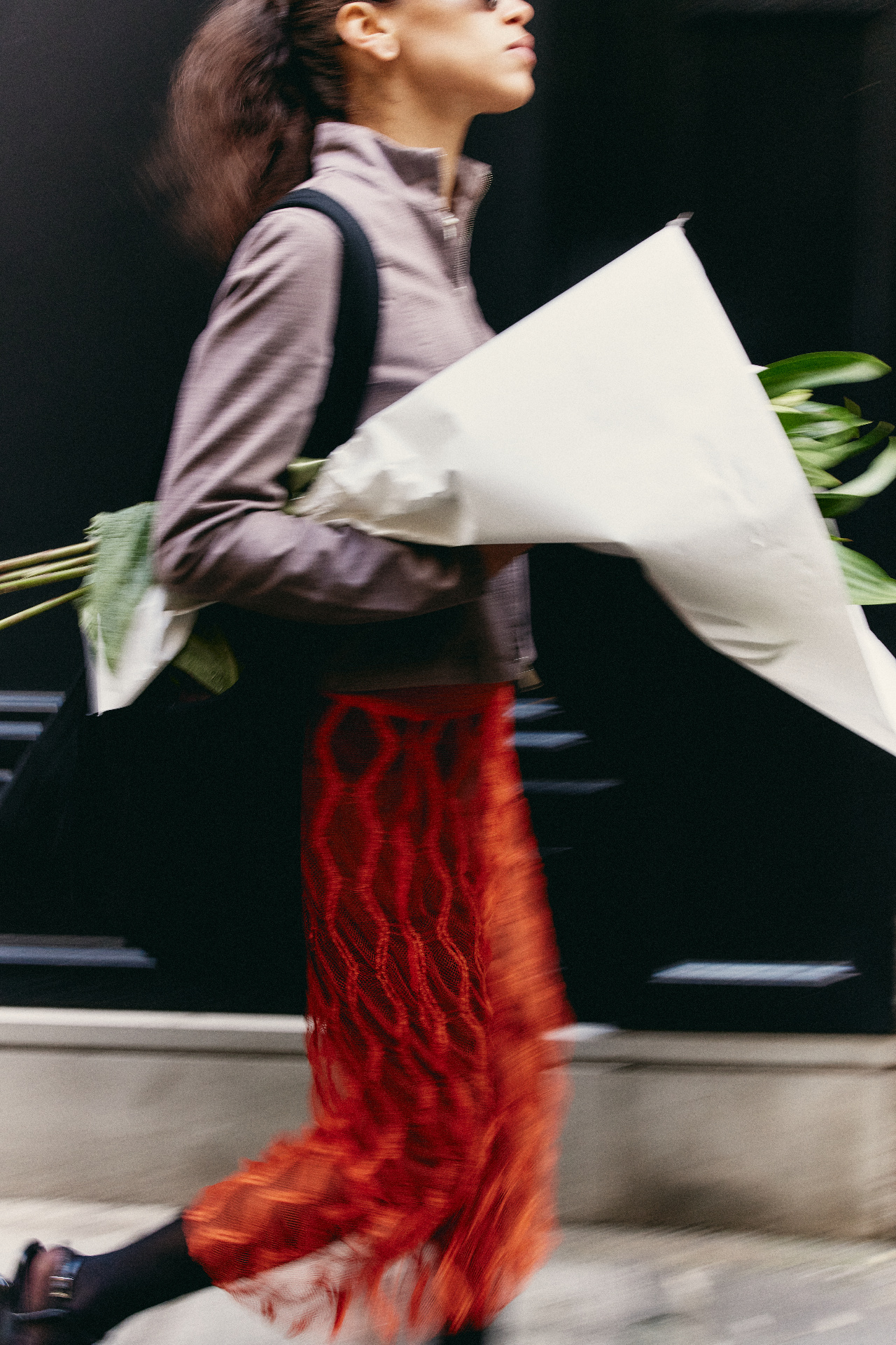 A woman in a red skirt walking with a bouquet of flowers wrapped in paper