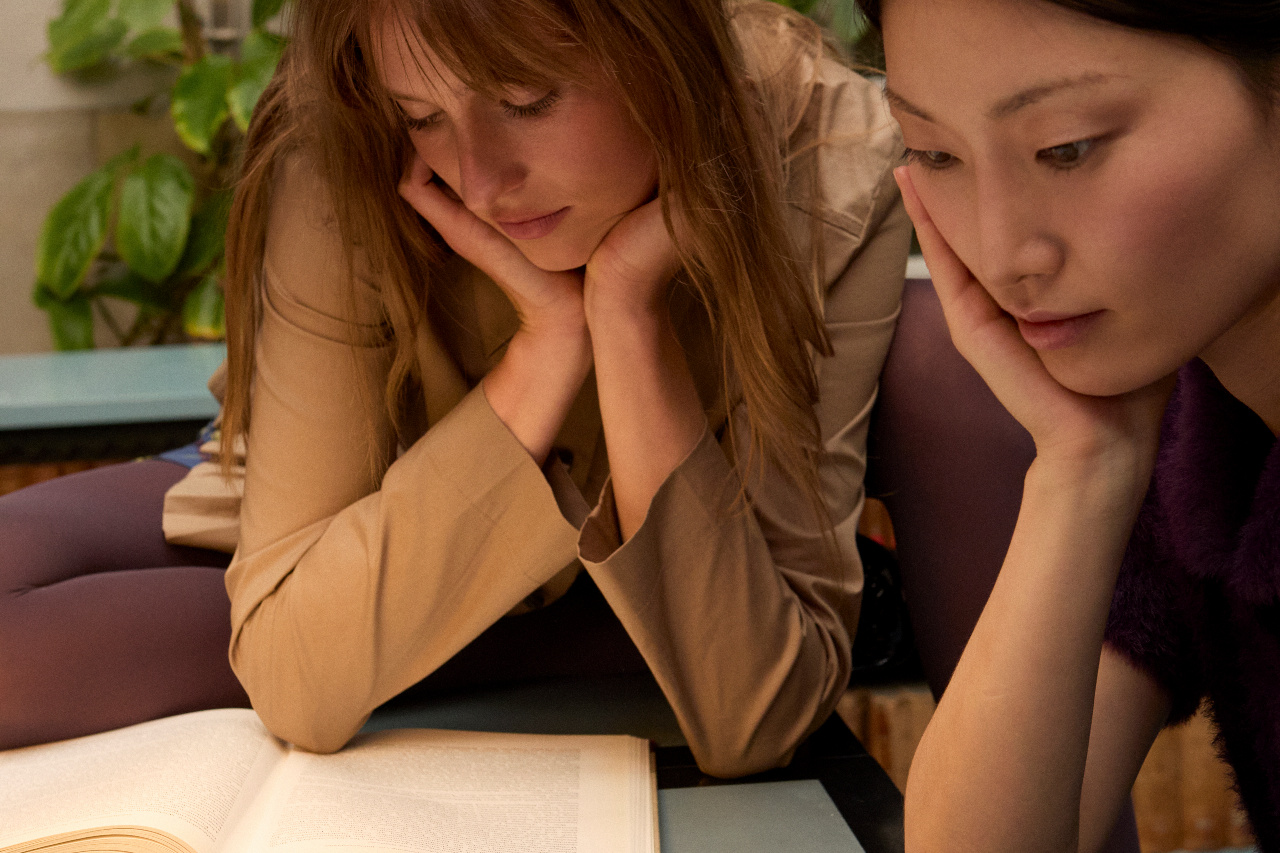 Two women resting their chins on their hands, reading an open book together