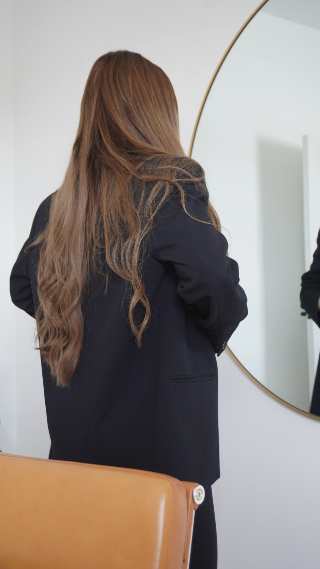 Woman in a black blazer studying her reflection in a round mirror