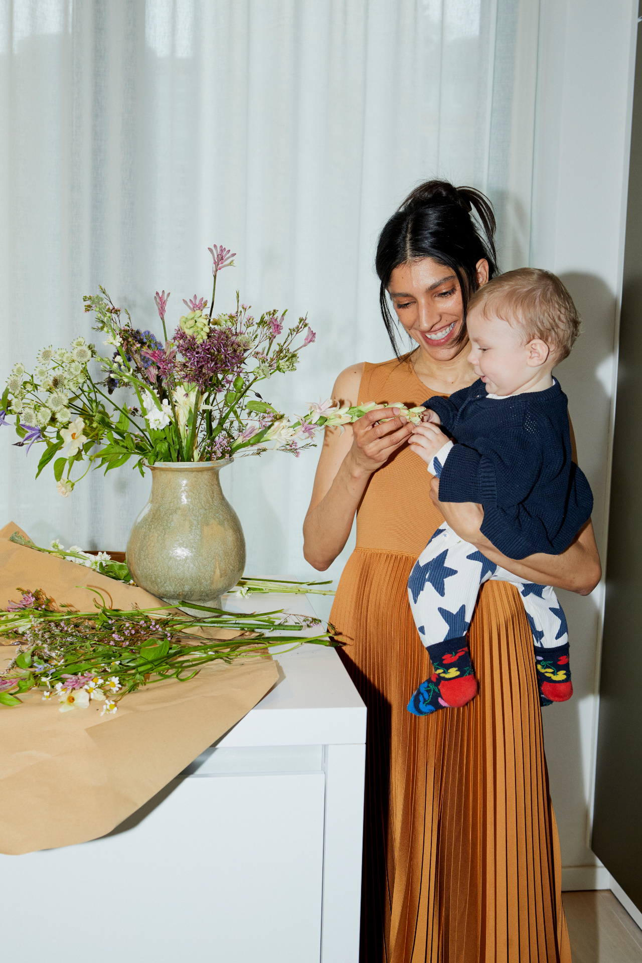 A smiling mother holding her baby beside a vase of fresh flowers