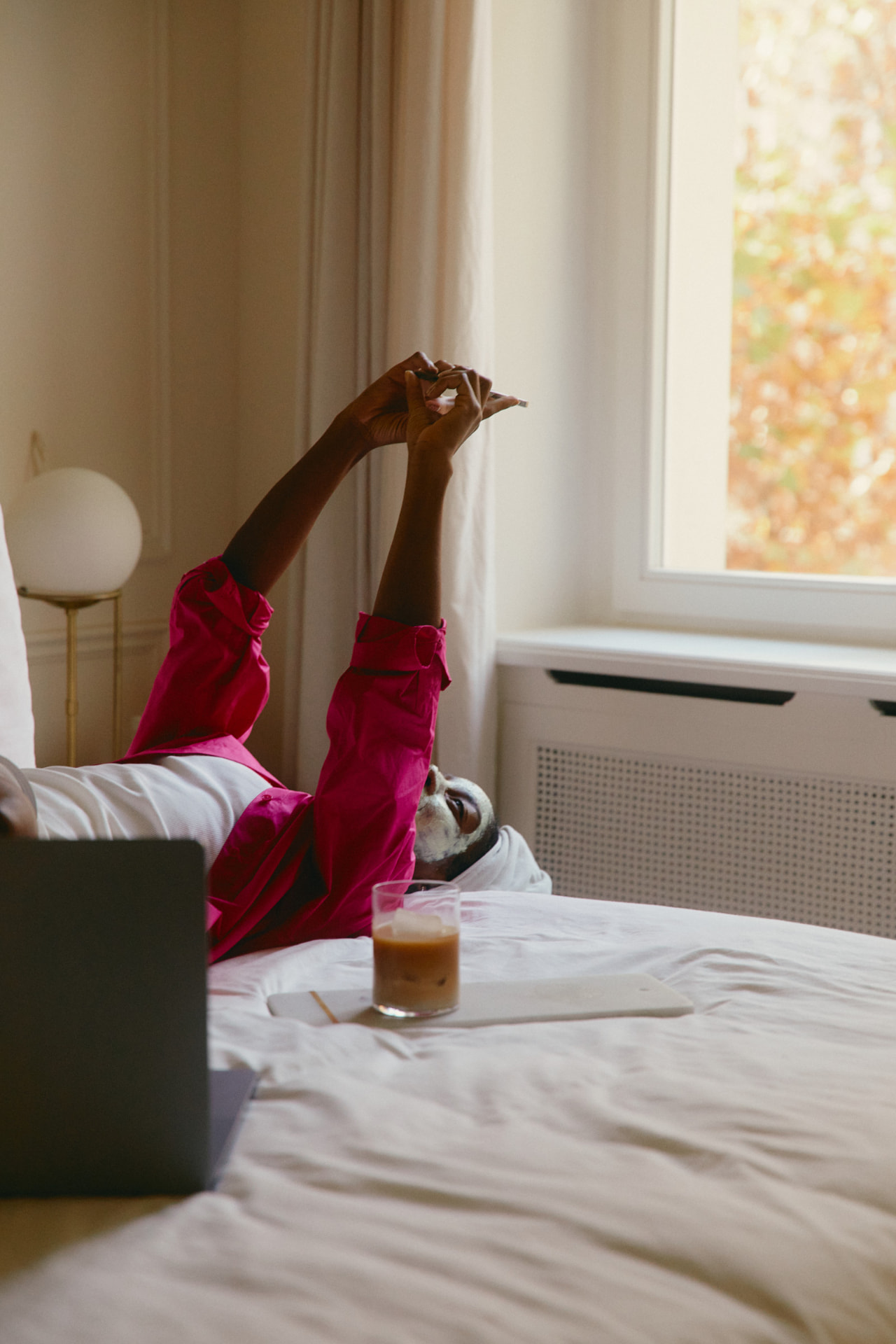 A woman in a hot pink shirt relaxing on a bed with a face mask, building income on her own terms