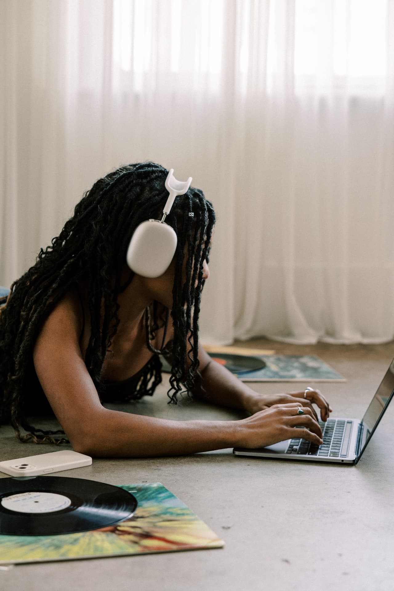Woman with dreadlocks working on a laptop wearing white headphones
